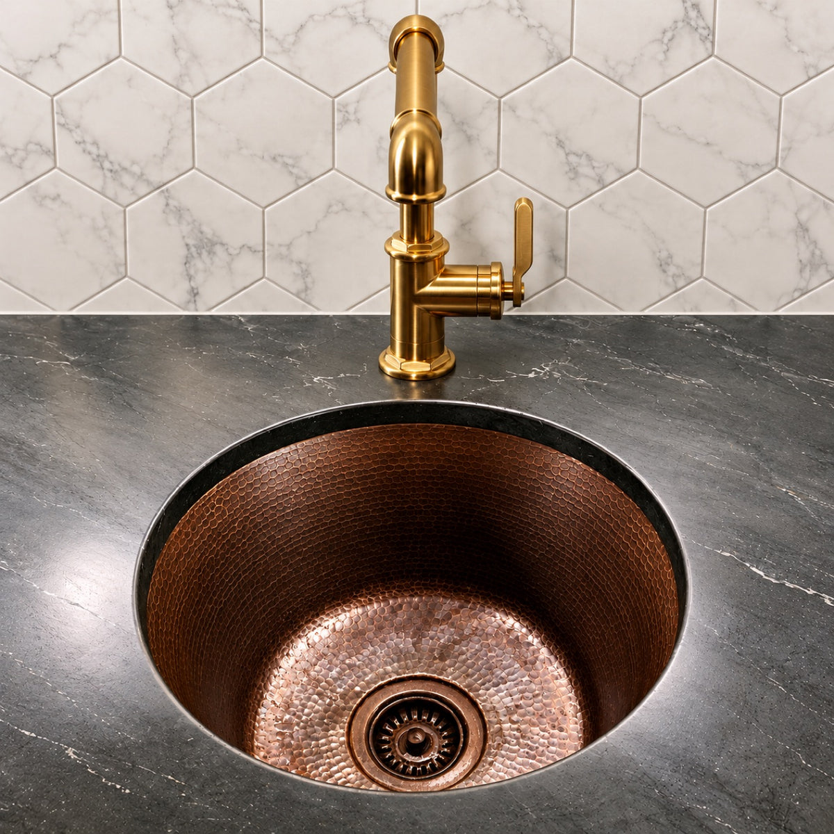Round hammered antique copper bar sink undermounted in a black marble counter, front view with brass faucet