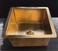Square hammered brass bar sink with polished unlacquered living finish on a black background