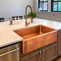 Hammered copper farmhouse kitchen sink installed in a white kitchen with a copper faucet